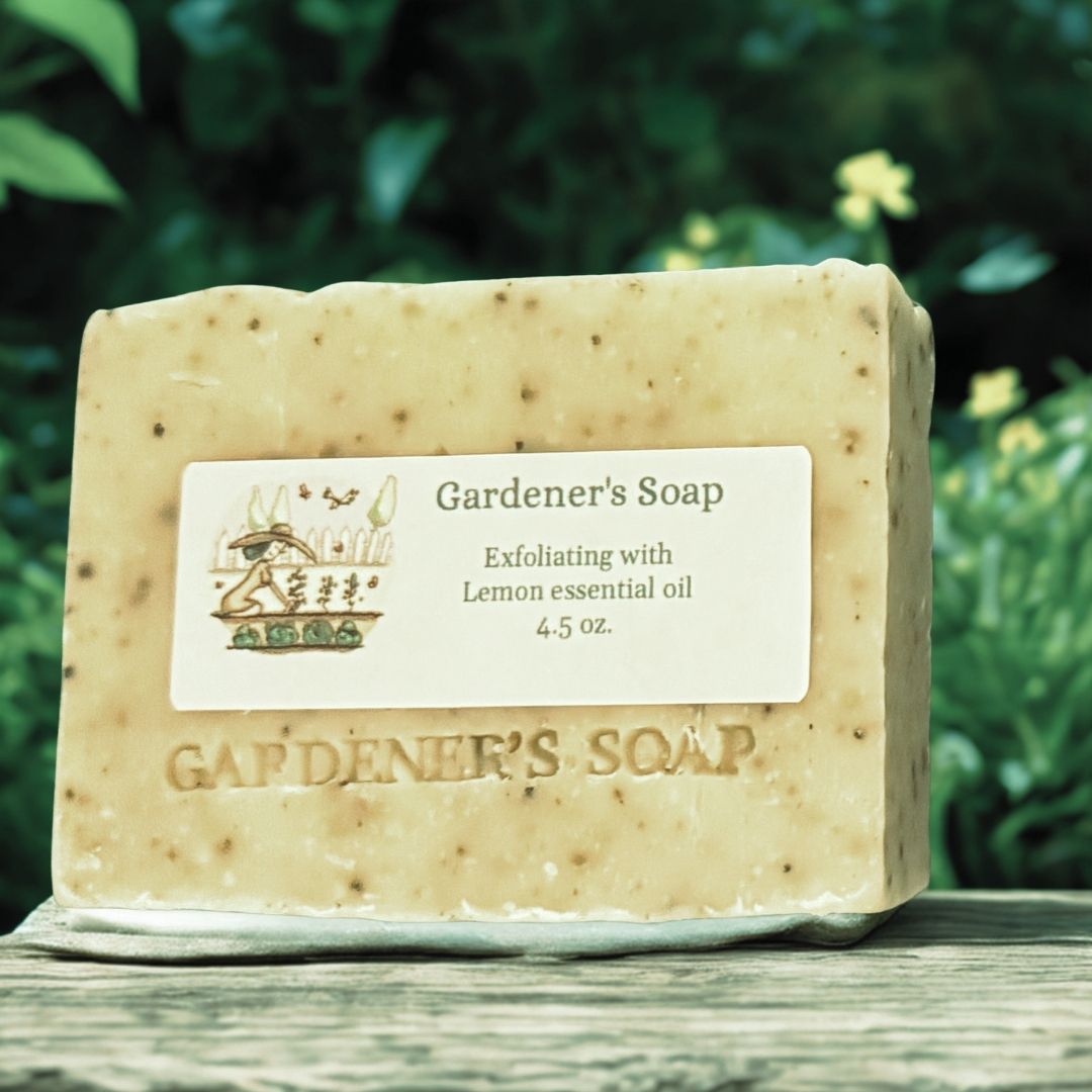 A rectangular bar of exfoliating lemon scented Gardener's Soap resting on a weathered wooden surface with a blurred green garden background.