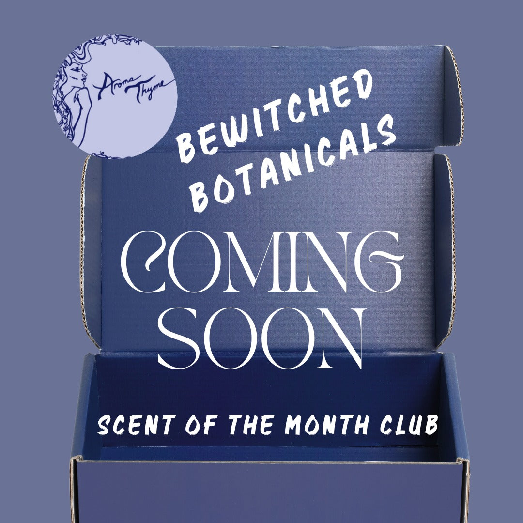 An open dark blue cardboard box with white text reading 'Bewitched Botanicals Coming Soon' and 'Scent of the Month Club' on a muted blue-gray background. A circular logo sticker for 'Aroma Tigris' appears in the upper left.